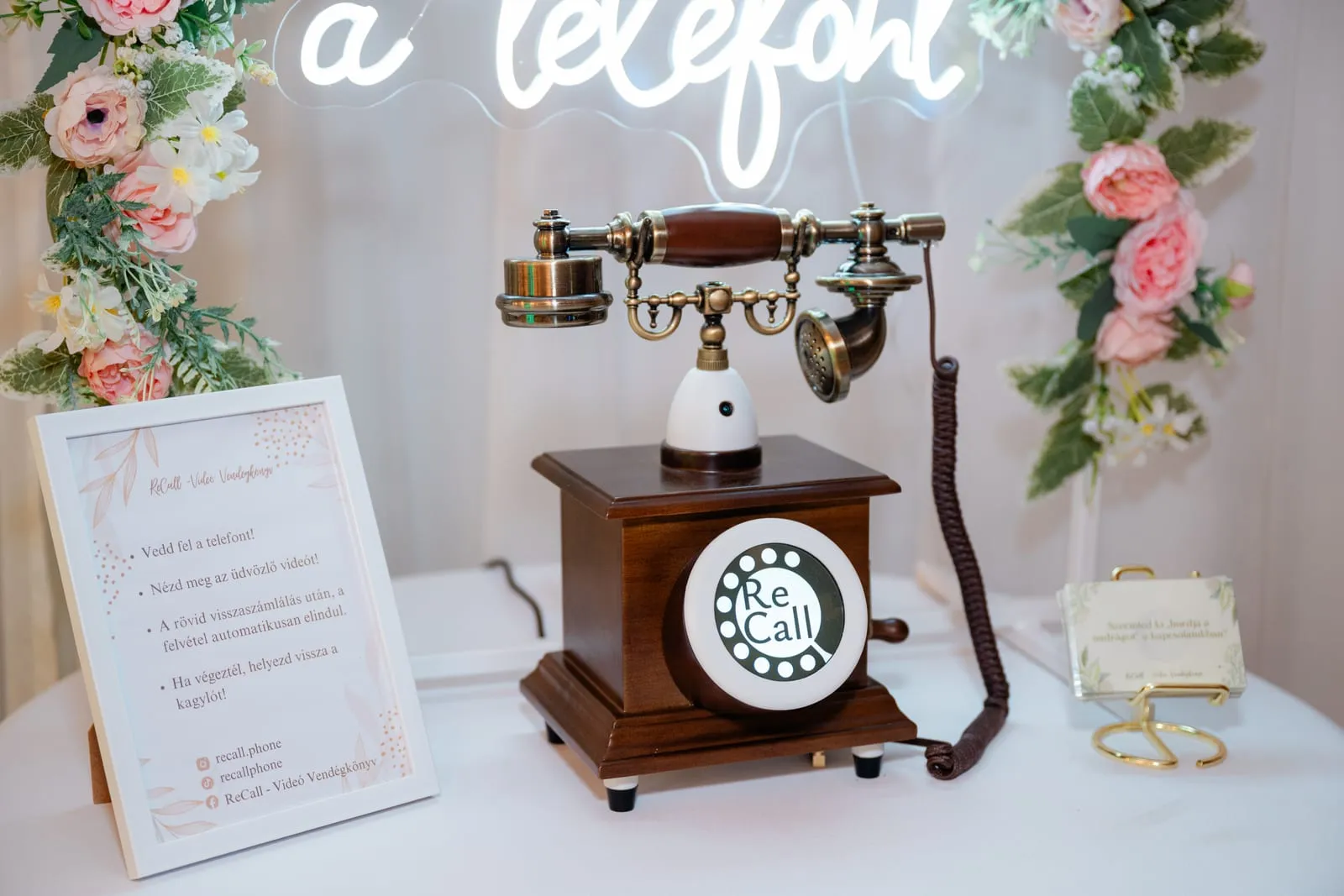 Az Ezüst csomag: vintage ReCall telefon keretezett útmutató táblával és kérdéskártyával, virágos dekoráció előtt